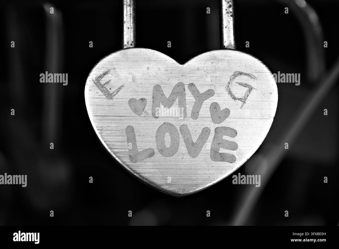 Ein verwittertes rosa herzförmiges Schild mit den Worten "MEINE LIEBE" hängt an Metallstäben und hebt sich von einem warmen, sanft verschwommenen Hintergrund ab. Stockfoto