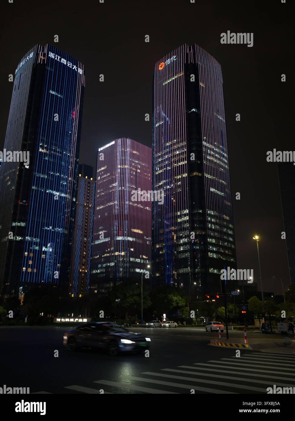 LED-beleuchtete Bürotürme über einer Straßenkreuzung mit einem verschwommenen Auto bei Nacht. Stockfoto