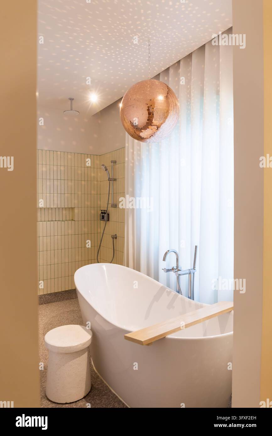 Weiße Badewanne mit warmem Licht gegen einen Warm- und Kaltwasserhahn und einer Holztafel zur Aufbewahrung Stockfoto
