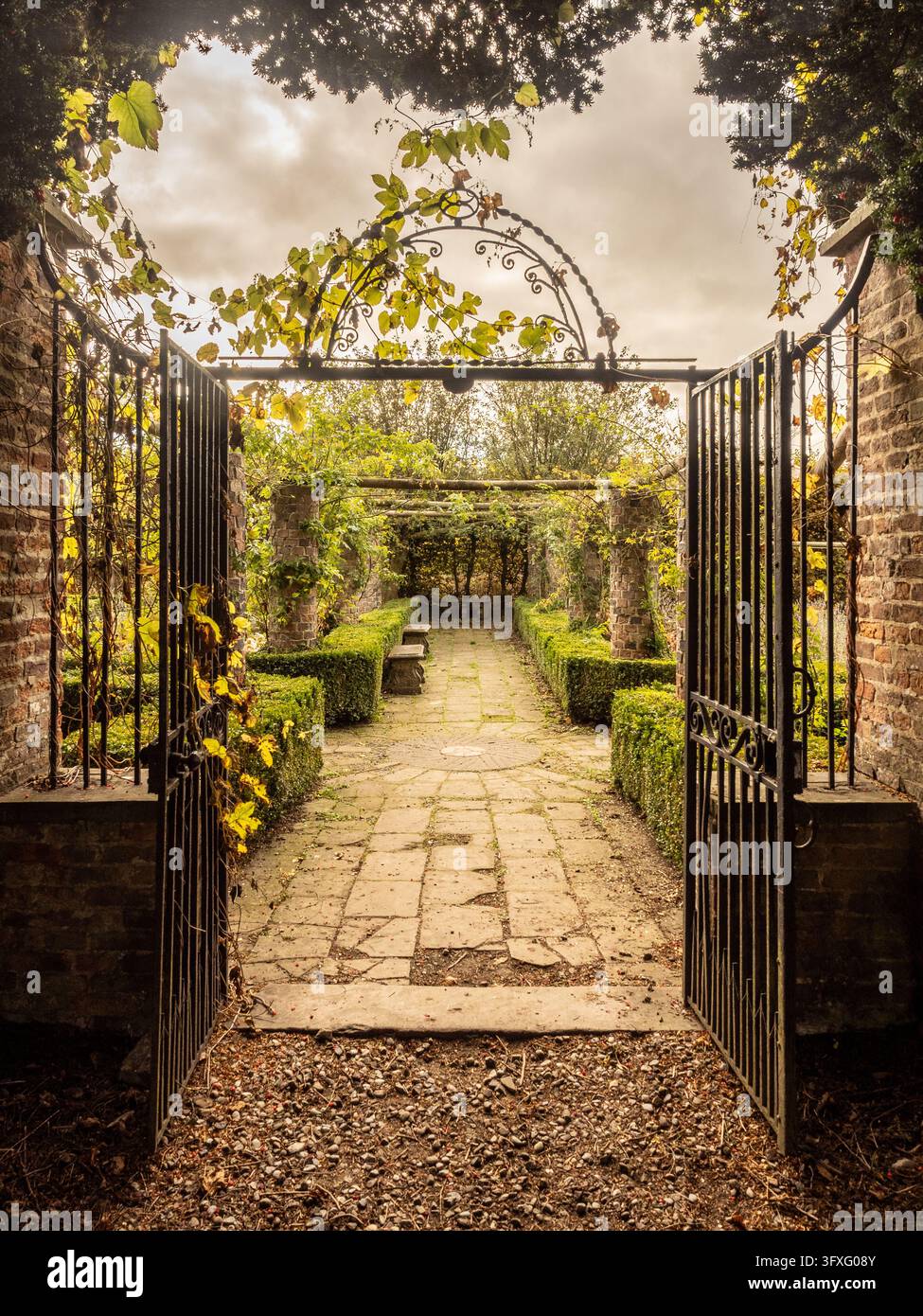 Zier schmiedeeiserne Tore öffnen sich zu einem Steinweg unter einer Pergola im Garten von Ripley Castle, North Yorkshire, England. Stockfoto