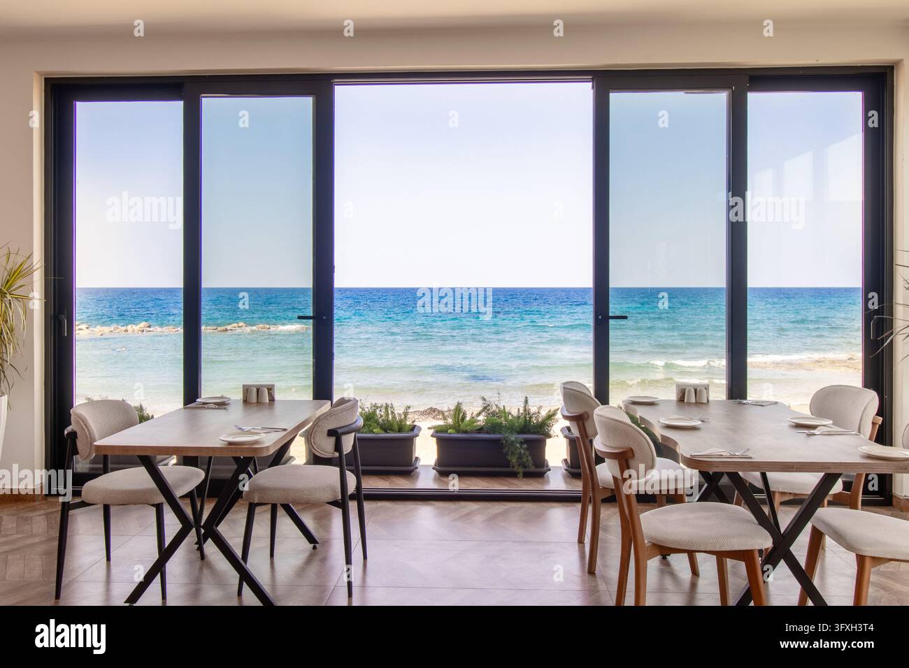 Modernes Restaurantinterieur mit einer wunderschönen Aussicht auf das blaue Meer und den türkisfarbenen Horizont. Tatlisu. Strandrestaurant Satin Bay Stockfoto