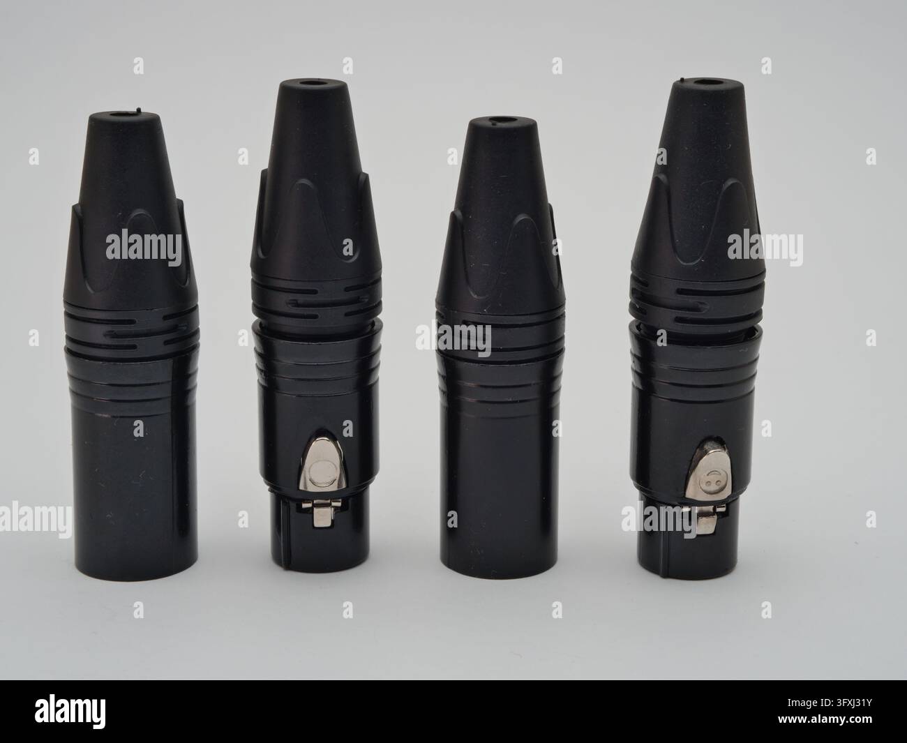 Schwarze XLR-Anschlüsse auf weißem Hintergrund – Vier schwarze XLR-Audioanschlüsse sind ordentlich in einer Reihe auf einem sauberen weißen Hintergrund angeordnet, um t Stockfoto