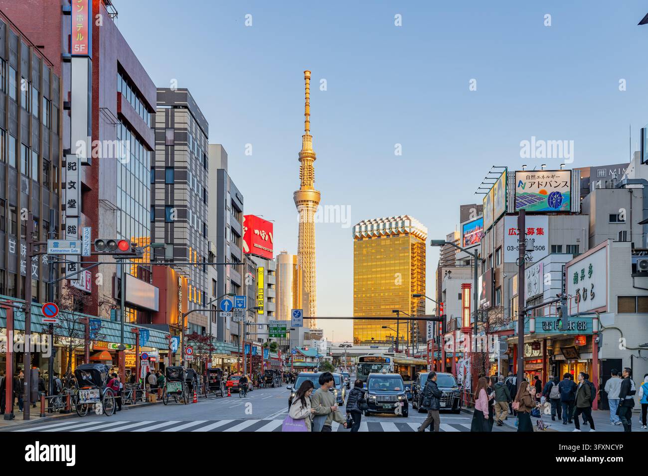 Tokio, Japan, 22. NOV 2024 - Fußgänger und Fahrzeuge bewegen sich durch eine belebte Straße in Asakusa, die mit Geschäften und Rikschas gesäumt ist, während der Tokyo Skytree in den Himmel ragt Stockfoto