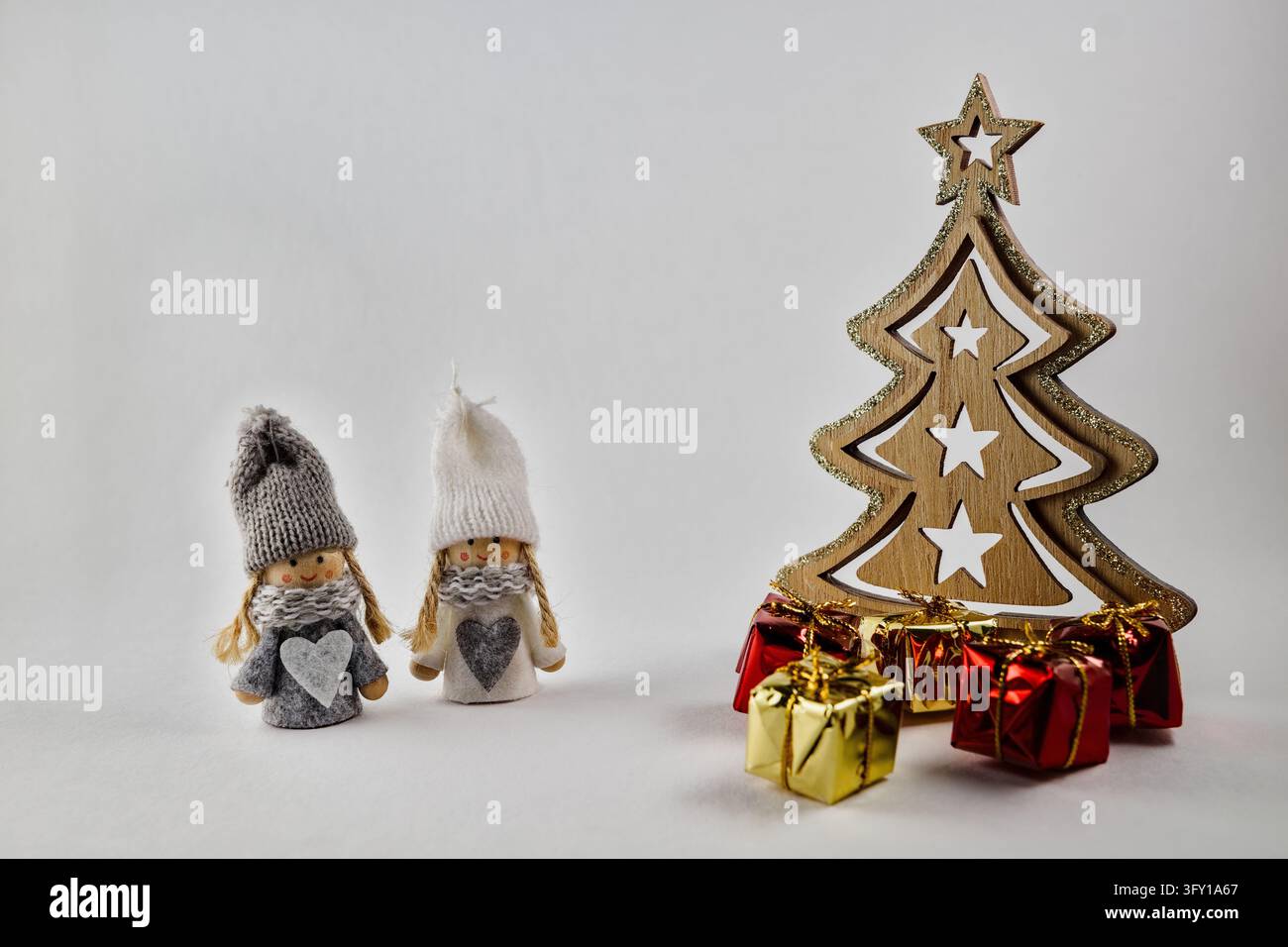 Zwei niedliche handgemachte Zwergpüppchen stehen neben einem geschnitzten Holz-Weihnachtsbaum und kleinen verpackten Geschenken. Stockfoto