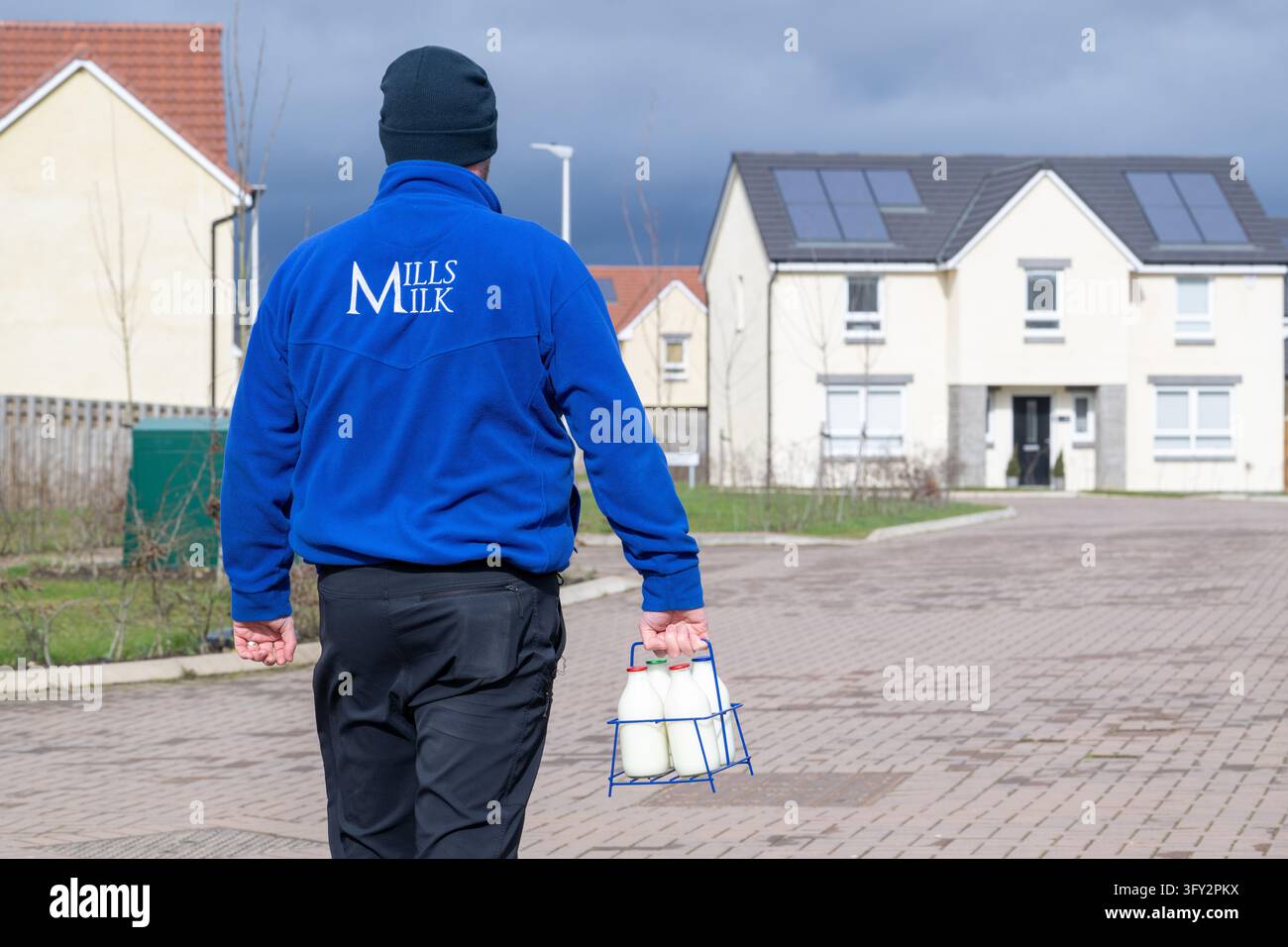 Ein Mills Milk-Lieferfahrer mit Glas-Milchflaschen und Lieferwagen in einer David Wilson Homes-Siedlung, Schottland, UK Stockfoto