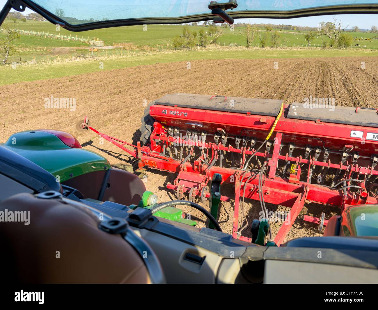 Rote Sämaschine sät Feld, gesehen aus der Kabine eines John-Deere-Traktors Stockfoto