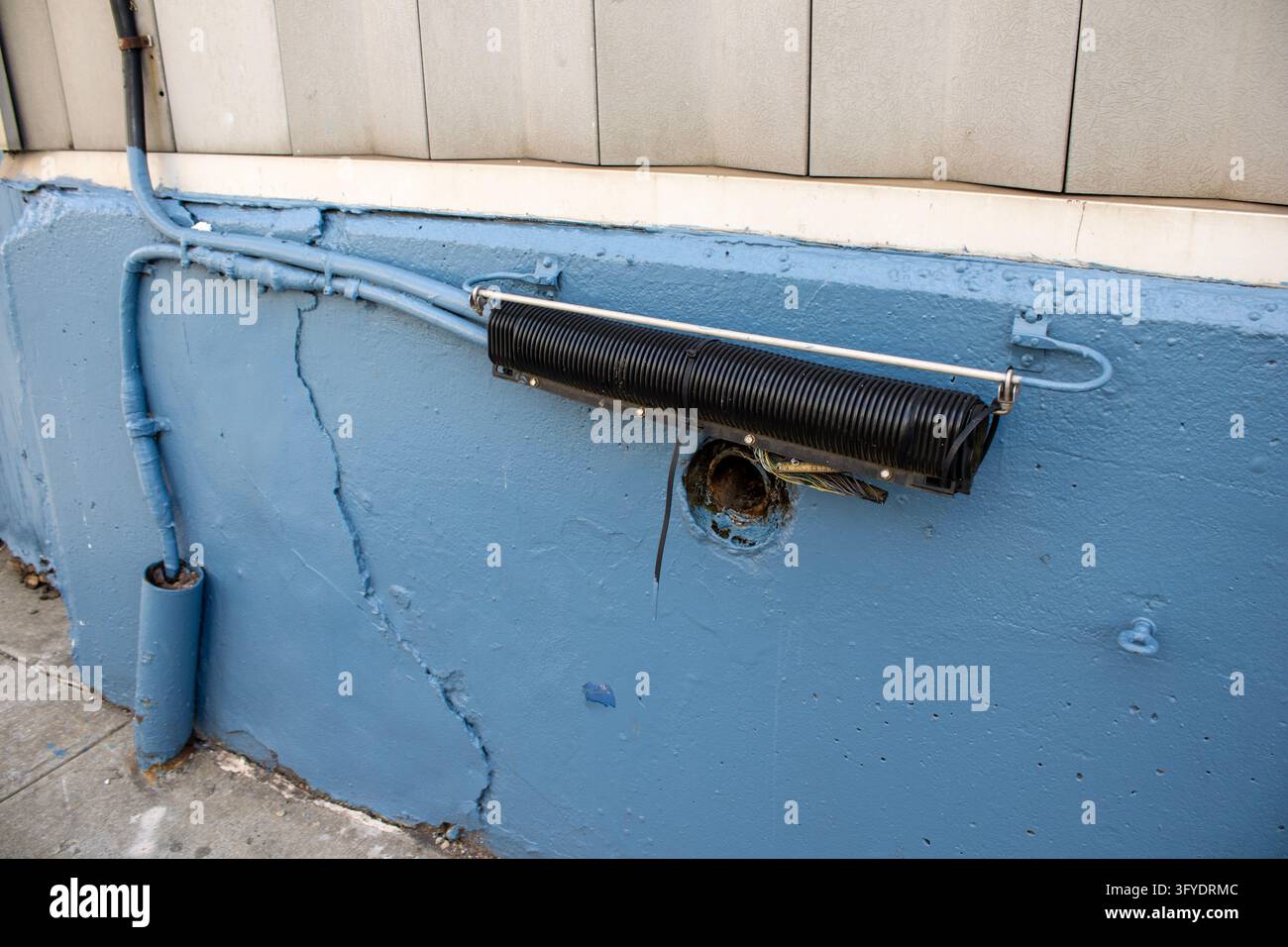 New York City, USA – 19. März 2024: Alte schwarze Leitung und rissige, abblätternde blaue Farbe an einer Betonwand am Pier 57. Stockfoto