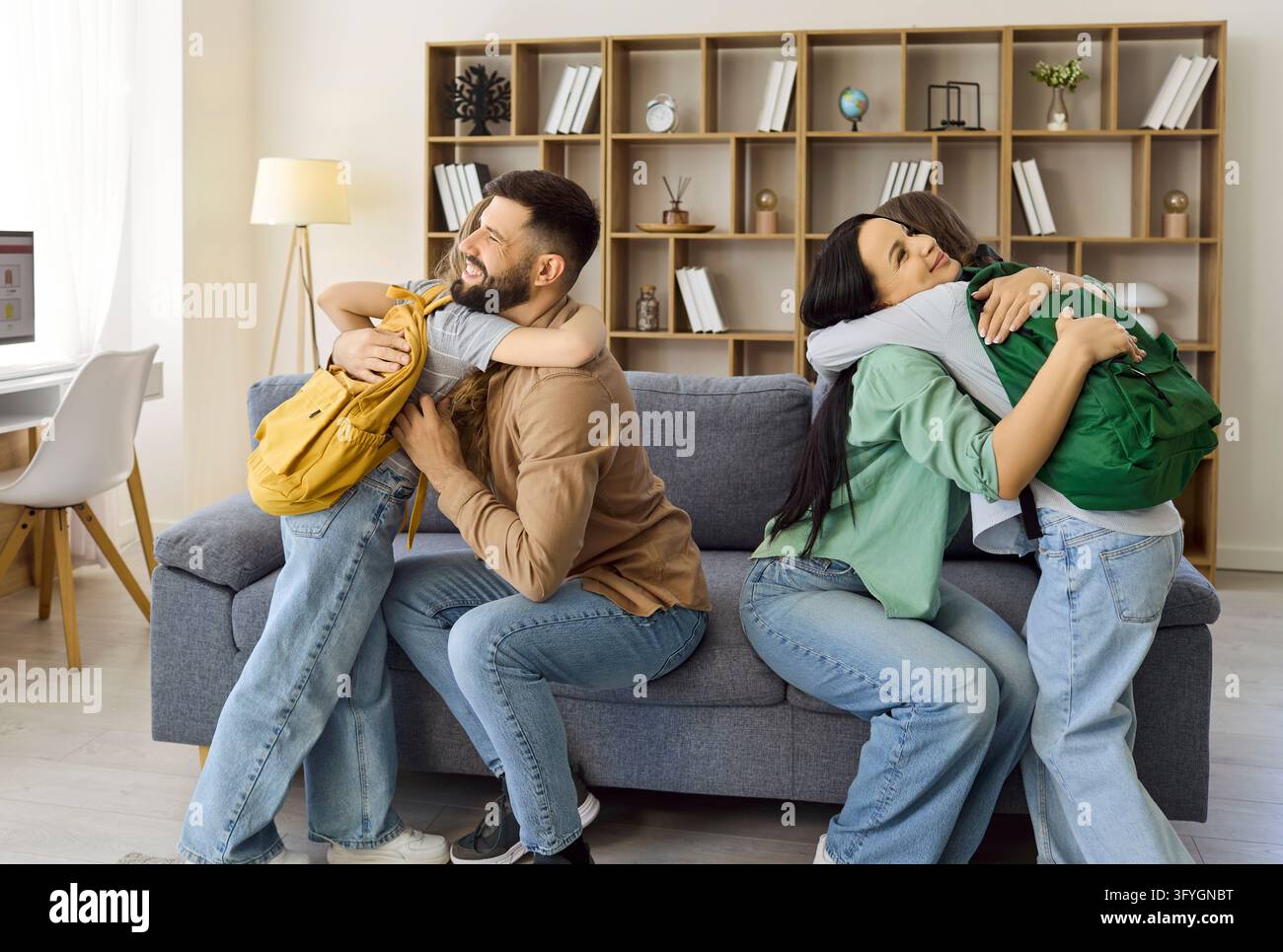 Eltern umarmen Schulkinder mit Rucksäcken vor der Schule in einem gemütlichen Wohnzimmer zu Hause Stockfoto