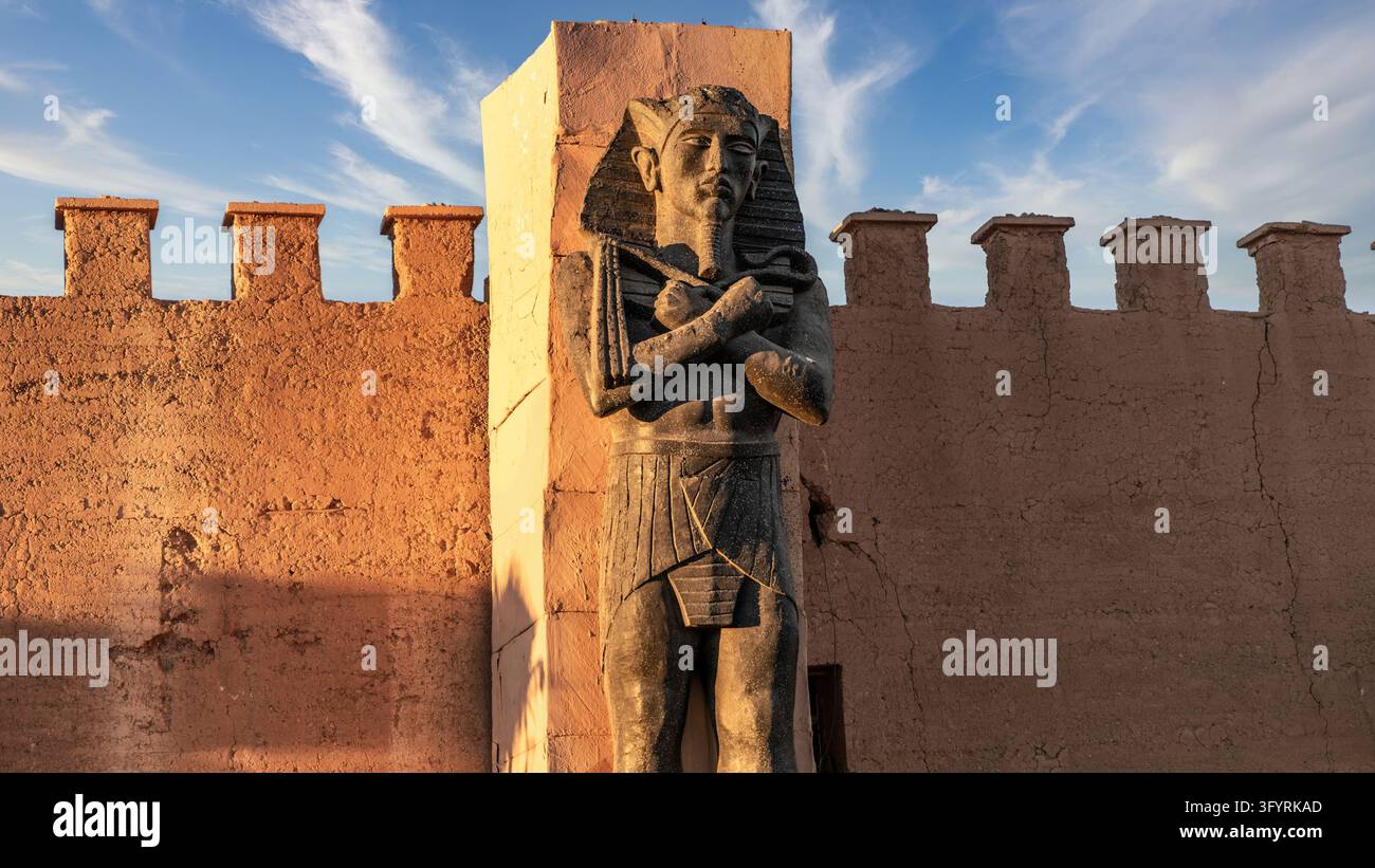 Ouarzazate, Marokko - 14. September 2022: Ägyptische Pharao-Statue im ägyptischen Stil mit gekreuzten Armen vor zackigen Lehmwänden im Filmmuseum in Oua Stockfoto