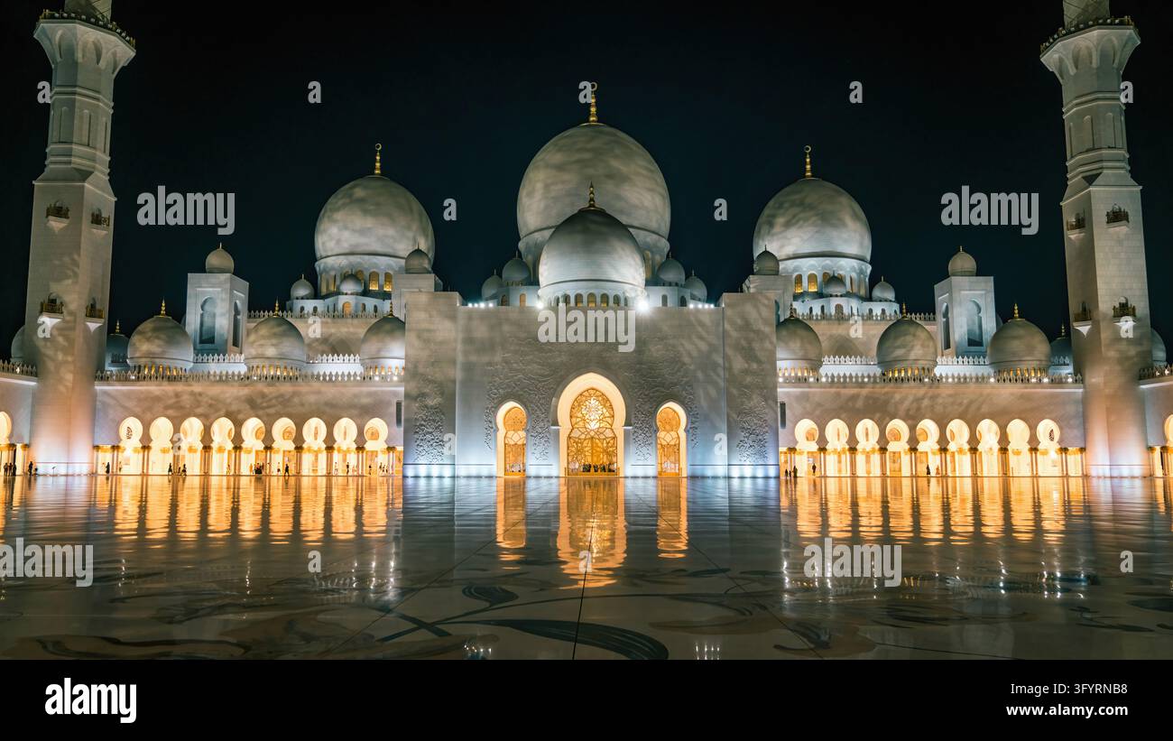 Abu Dhabi, UAE - 18. Februar 2022: Scheich-Zayed-Großmoschee bei Nacht beleuchtet, ihre weißen Marmordome, Minarette und goldenen Bögen spiegeln sich im Stockfoto