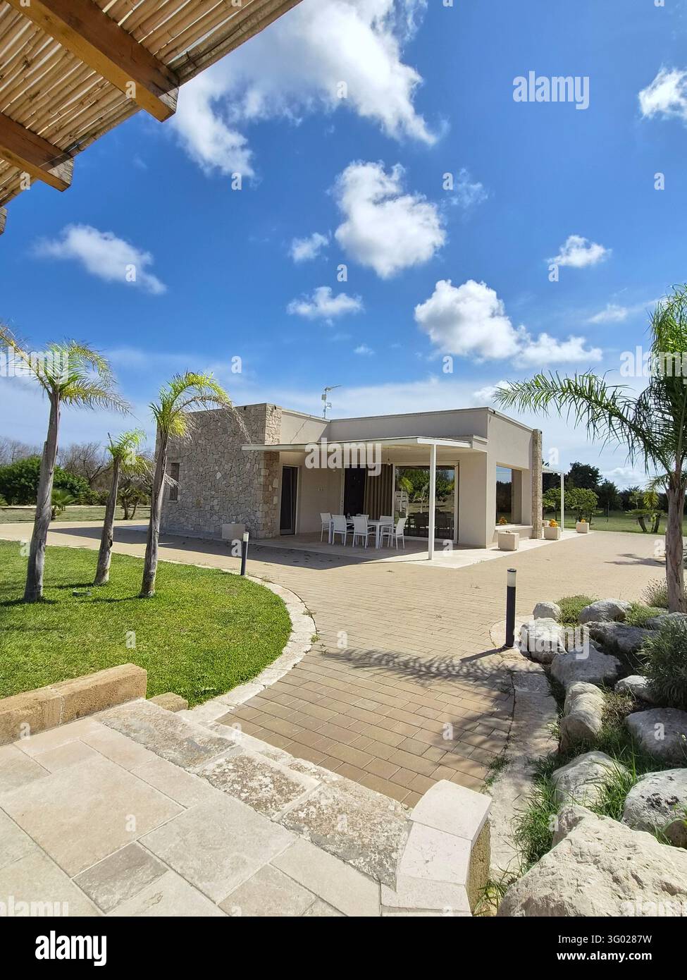 Moderne steinerne Ferienvilla mit Terrasse, Palmen und Garten in Salento, Apulien, Italien, September 2026 - Smartphone-aufgenommenes Stockfoto