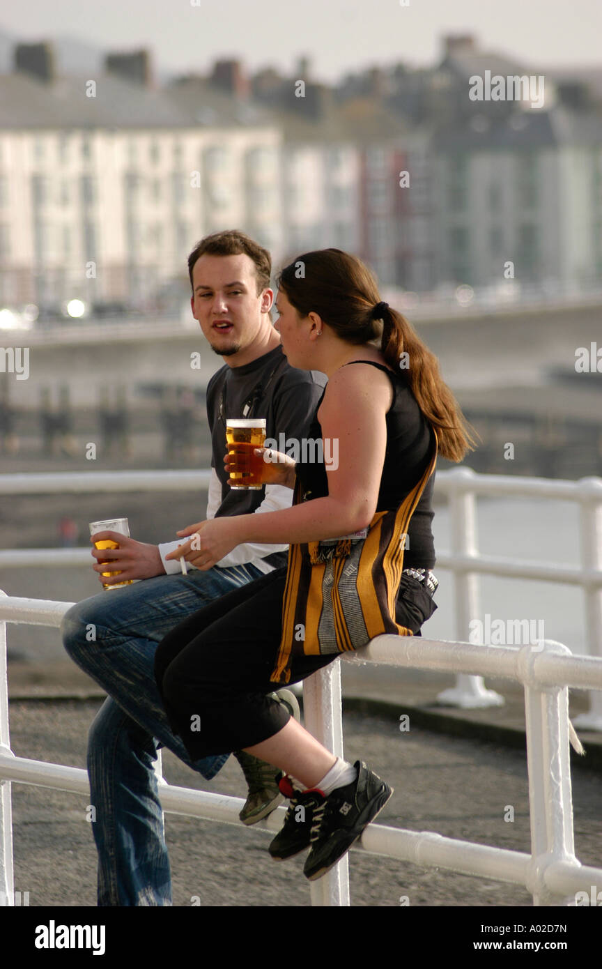 Junges Paar - Universitätsstudenten - sitzen am Meer Geländer Aberystwyth promenade Sommer Abend trinken Pints Bier Stockfoto