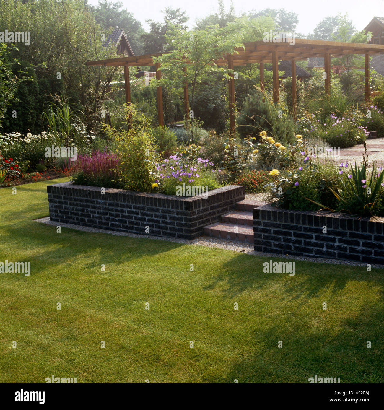 Rasen vor Treppe zur Terrasse mit Hochbeeten und Pergola im Garten