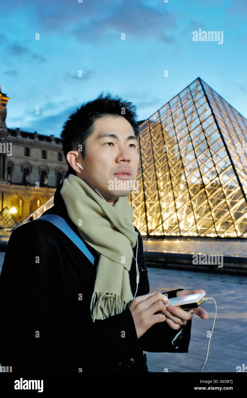 Paris Frankreich, Portrait junger asiatischer Mann, der nachts MP3-Player mit Kopfhörern in der Nähe der Pyramide des Louvre-Museums hört Stockfoto