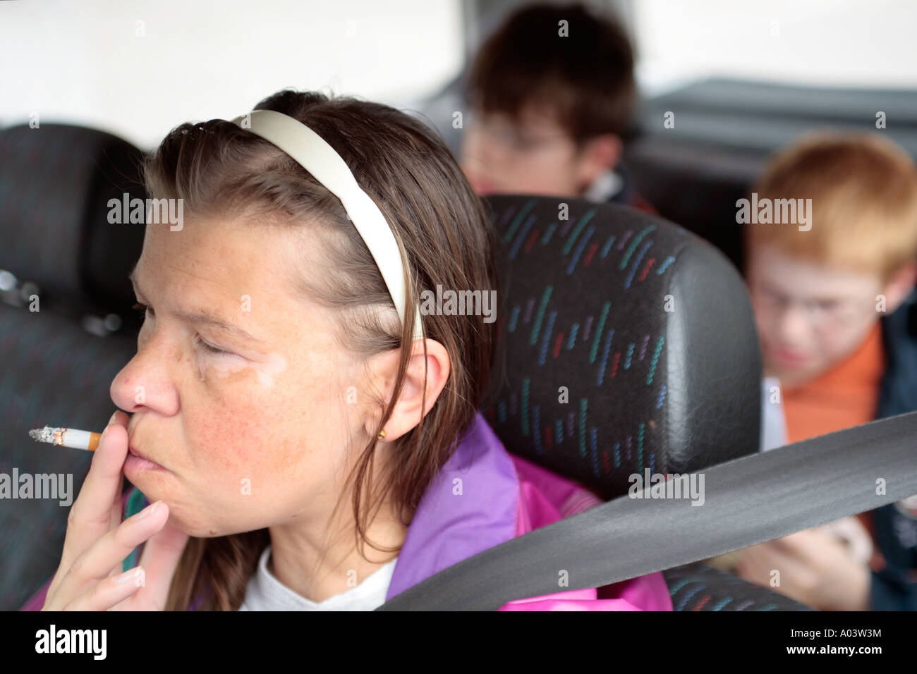 eine Mutter, die das Rauchen während der Fahrt mit ihren kleinen Söhnen auf der Rückseite ihres Autos Stockfoto