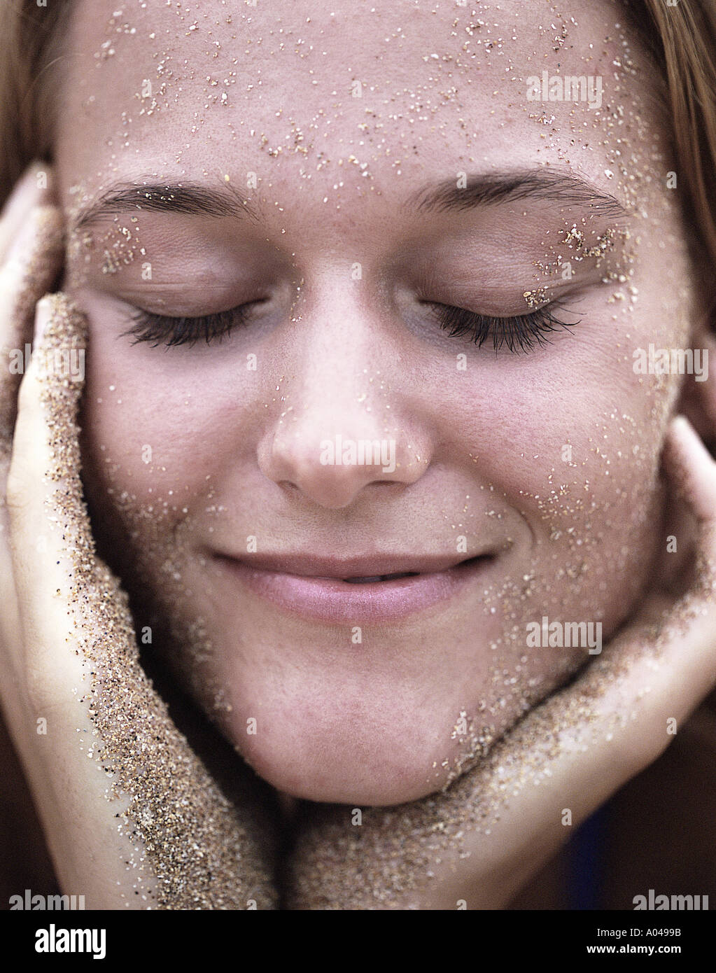 Porträt einer jungen Frau mit Sand auf ihrem Gesicht lächelnd Stockfoto