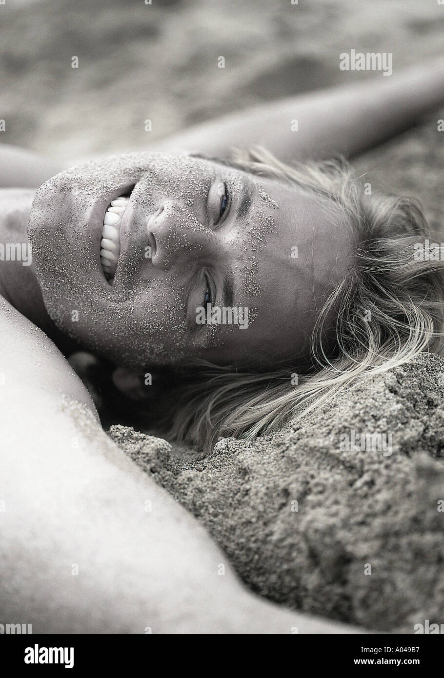 Junger Mann mit ausgestreckten Armen auf dem Rücken im Sand liegend lächelnd Stockfoto