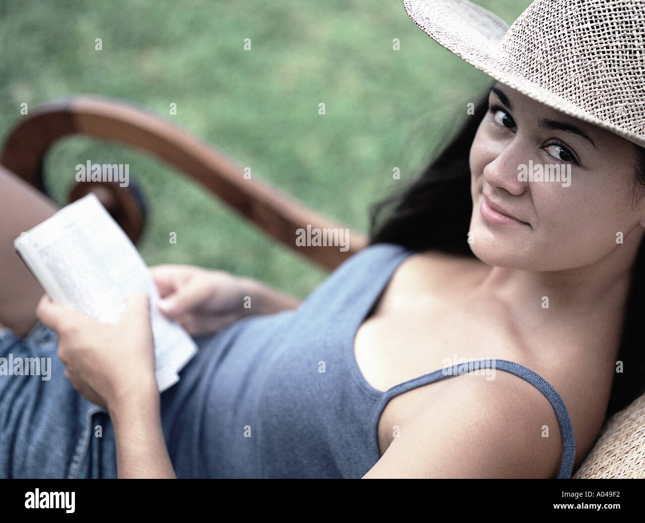 Junge Frau sitzt im Freien in einem Stuhl schaut in die Kamera hält ein Buch Stockfoto