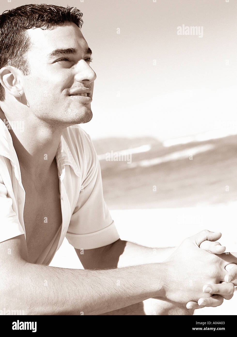 Porträt eines jungen Mannes trägt ein weißes aufgeknöpft Hemd am Strand sitzen Stockfoto