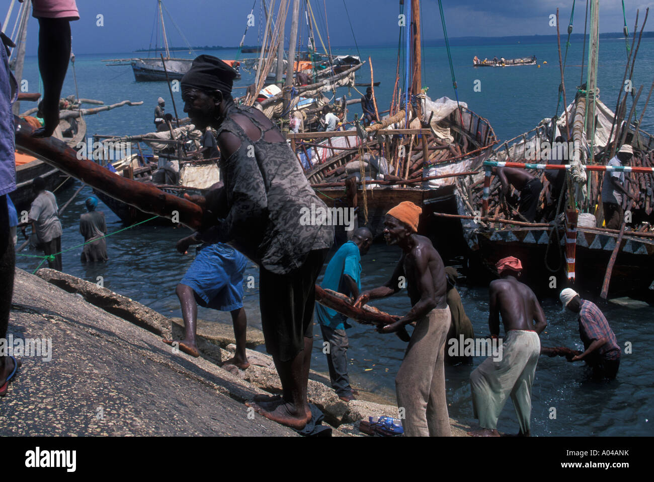 Afrika, Tansania, Zanzibar, Stone Town, Linie der Arbeiter entladen traditionellen Dhau Boot voller Log Pole im Hafen Stockfoto