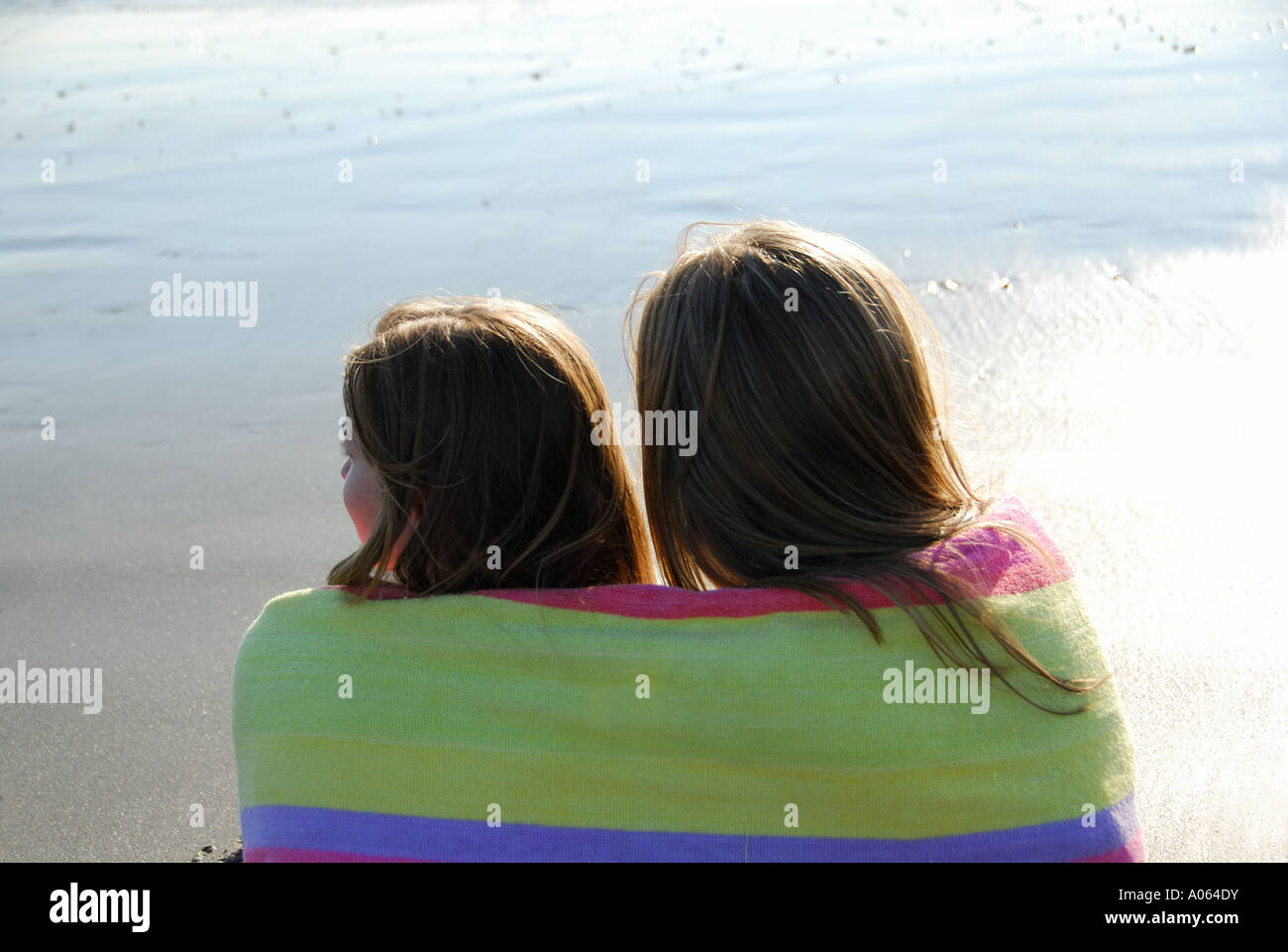 zwei Schwestern sitzen am Strand zusammen mit Handtuch umwickelt sie Stockfoto