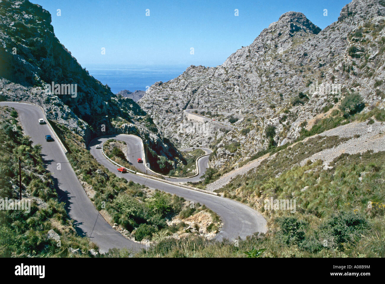 Von oben ein paar Autos, die ihren Weg entlang der kurvigen Bergstraße die ein Gestrüpp bedeckt Hang über Serpentinen hinunter zum Hafen in der Bucht von Sa Calobra auf der Nordküste von Mallorca schlängelt gesehen Stockfoto