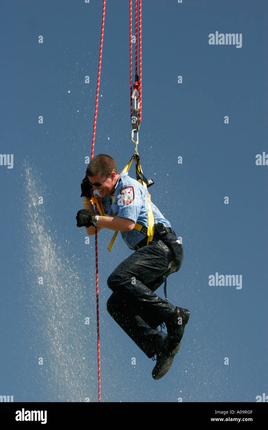 Ein Feuerwehrmann ist dabei die Antenne Seile und zum Spaß seinen Teamkollegen Bahnhof Spritzen ihn von unten aus einer Wasser-Maschinist Stockfoto