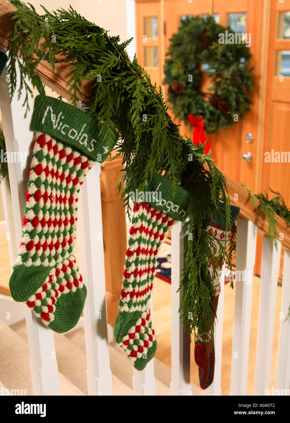 Weihnachtsstrümpfe aufgehängt auf Treppengeländer mit Tür und Kranz im Hintergrund Stockfoto