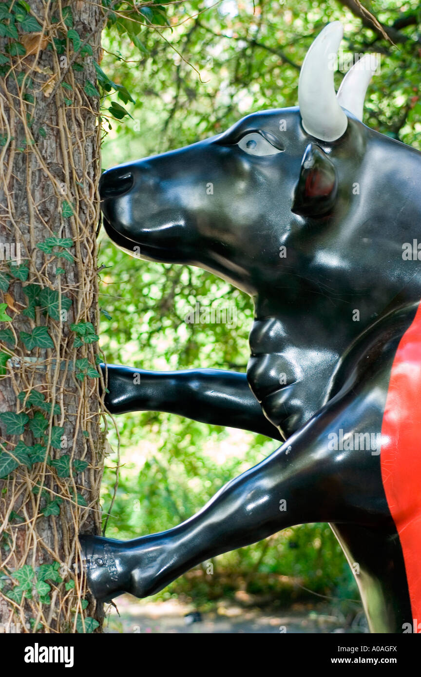 Roten und schwarzen Kunststoff Kuh von Cow Parade auf hinteren Beinen stehend und Baum zu berühren Stockfoto