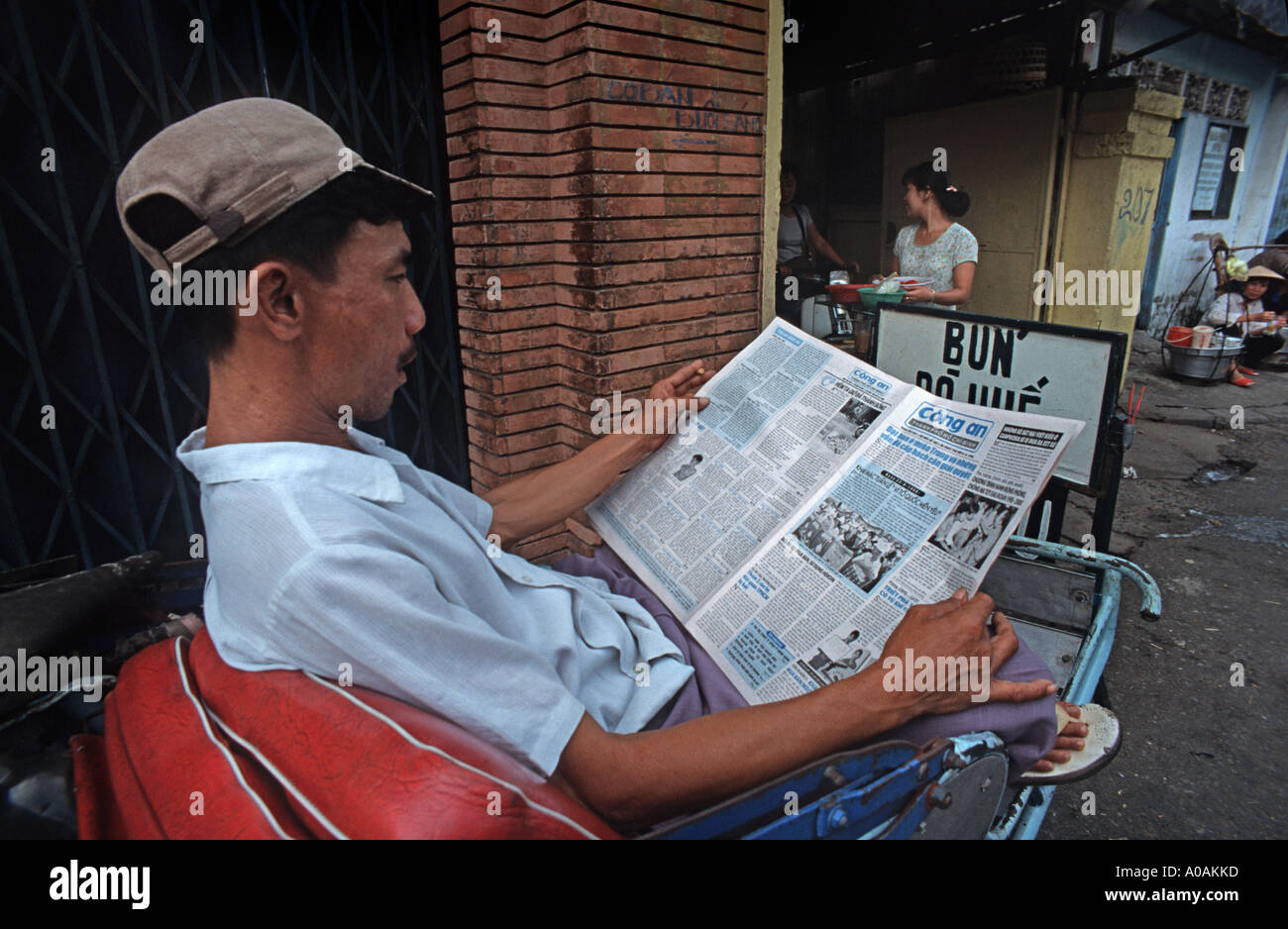 Eine Rikscha-Fahrer sitzt auf seinem Zyklus Lesen einer Tageszeitung Ho Chi Minh Stadt Saigon Vietnam Stockfoto