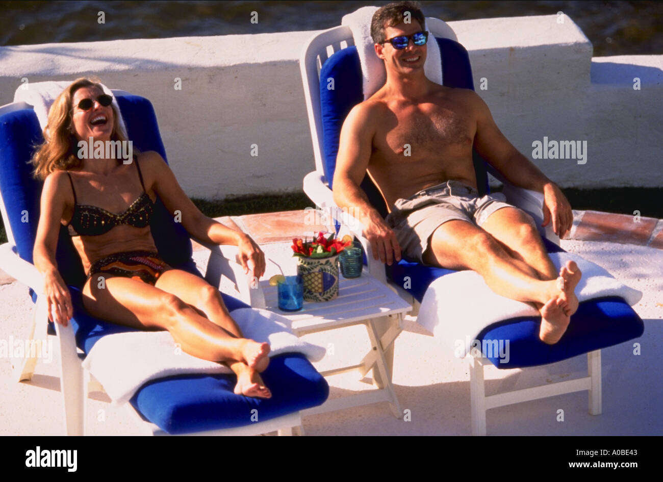 Mann und Frau tragen Swimsuites und Sonnenbaden in Liegestühlen und lachen Stockfoto