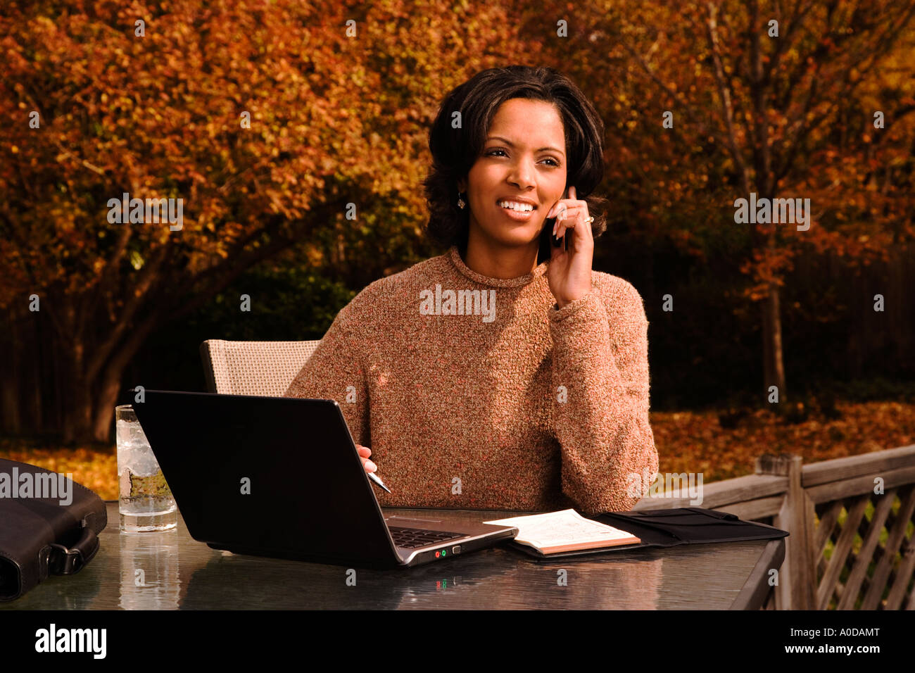 Afrikanische amerikanische Geschäftsfrau in Freizeitkleidung zu Hause mit einem Handy und Laptop-Computer außerhalb arbeiten Stockfoto