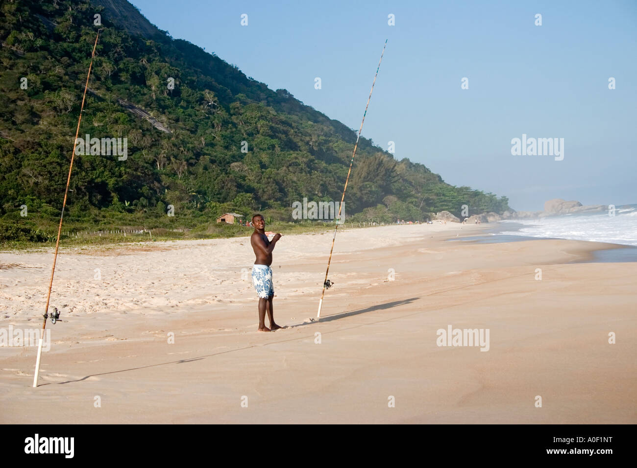 Schwarzer Mann Angeln mit 2 Angelruten am Strand von Grumari, Rio De Janeiro, Brasilien Stockfoto