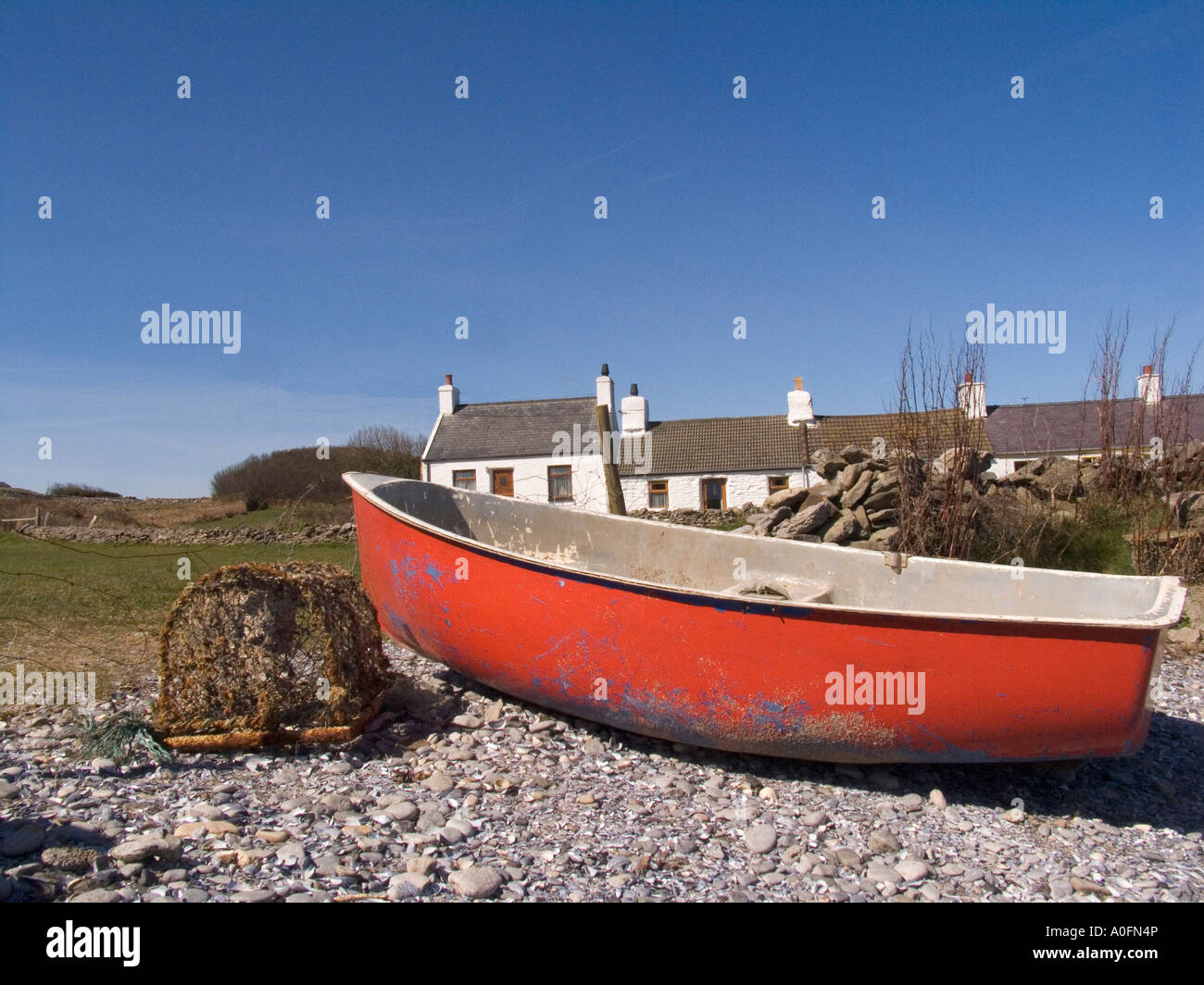 MOELFRE ISLE OF ANGLESEY NORTH WALES UK April A rot Rowing Boat ist mit einem alten verkrusteten Hummer Topf gestrandet. Stockfoto