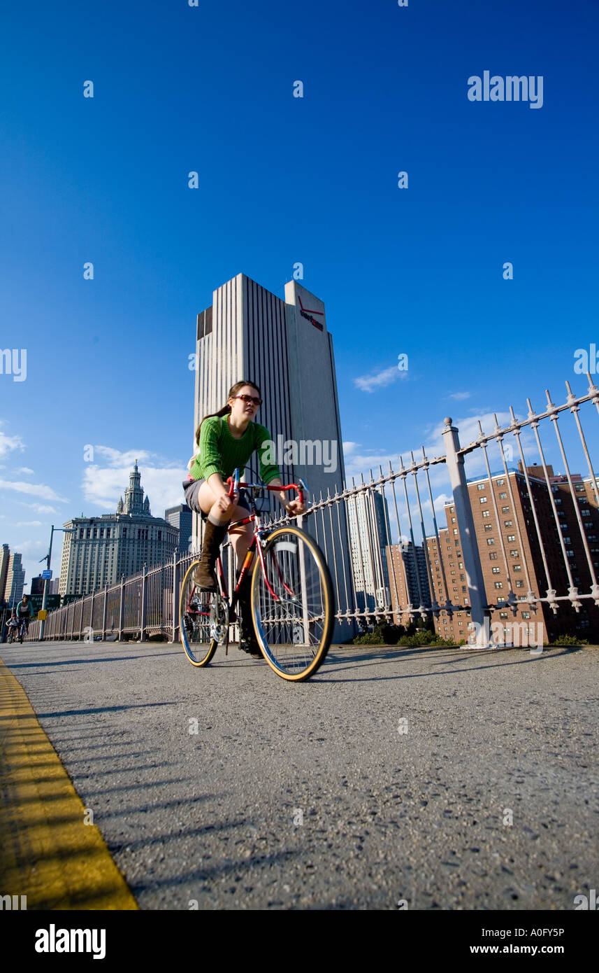 Mädchen Reiten Fahrrad auf der Brooklynbridge mit Hochhaus im Hintergrund Stockfoto