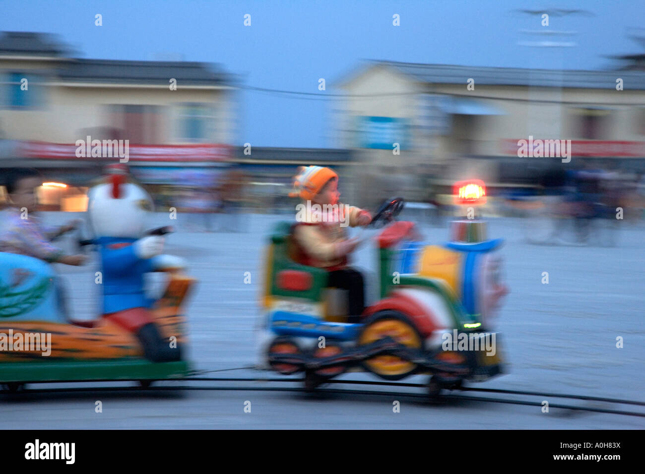 Kinder reiten Kiddie trainieren in Xinjie Dorfplatz in der Nacht, Yuanyang, Yunnan, China (Motion Blur) Stockfoto