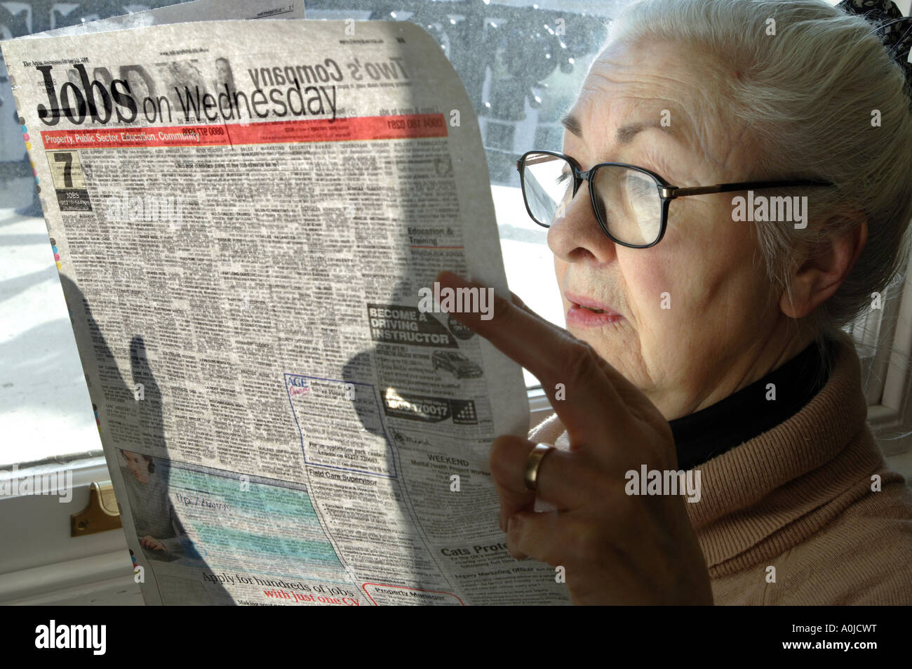 Nachdenklich aussehende Frau Rentner einen Überblick über die angebotenen Arbeitsplätze in ihrer Lokalzeitung. Stockfoto