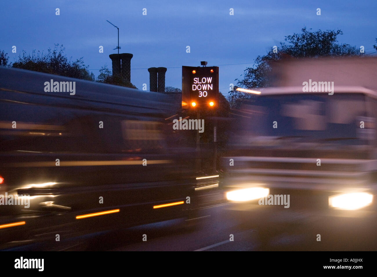 eine blinkende Geschwindigkeit Warnzeichen und schnell bewegenden Feierabendverkehr durch das Dorf große Barton in Suffolk, UK Stockfoto