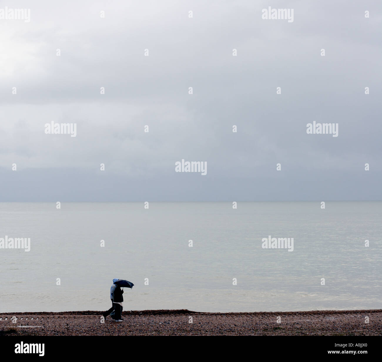 Kleine Figur mit Regenschirm zu Fuß am Strand Stockfoto