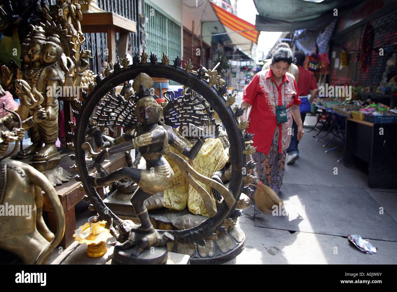 Eine Dame fegt vor ihr Geschäft in den Seitenstraßen von Phahurat das indische Viertel von Bangkok Thailand viele religiöse Artefakte in den Shop verkauft werden Stockfoto