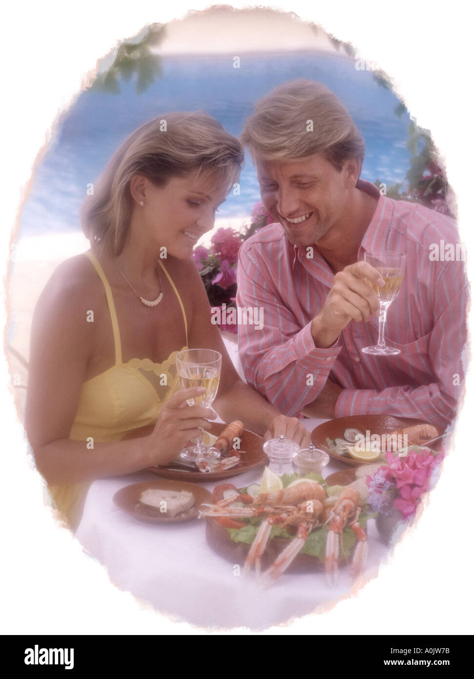 jung, Ehepaar mittleren Alters essen Meeresfrüchte im Abendlicht auf Terrasse mit Pool Oval vignette Stockfoto