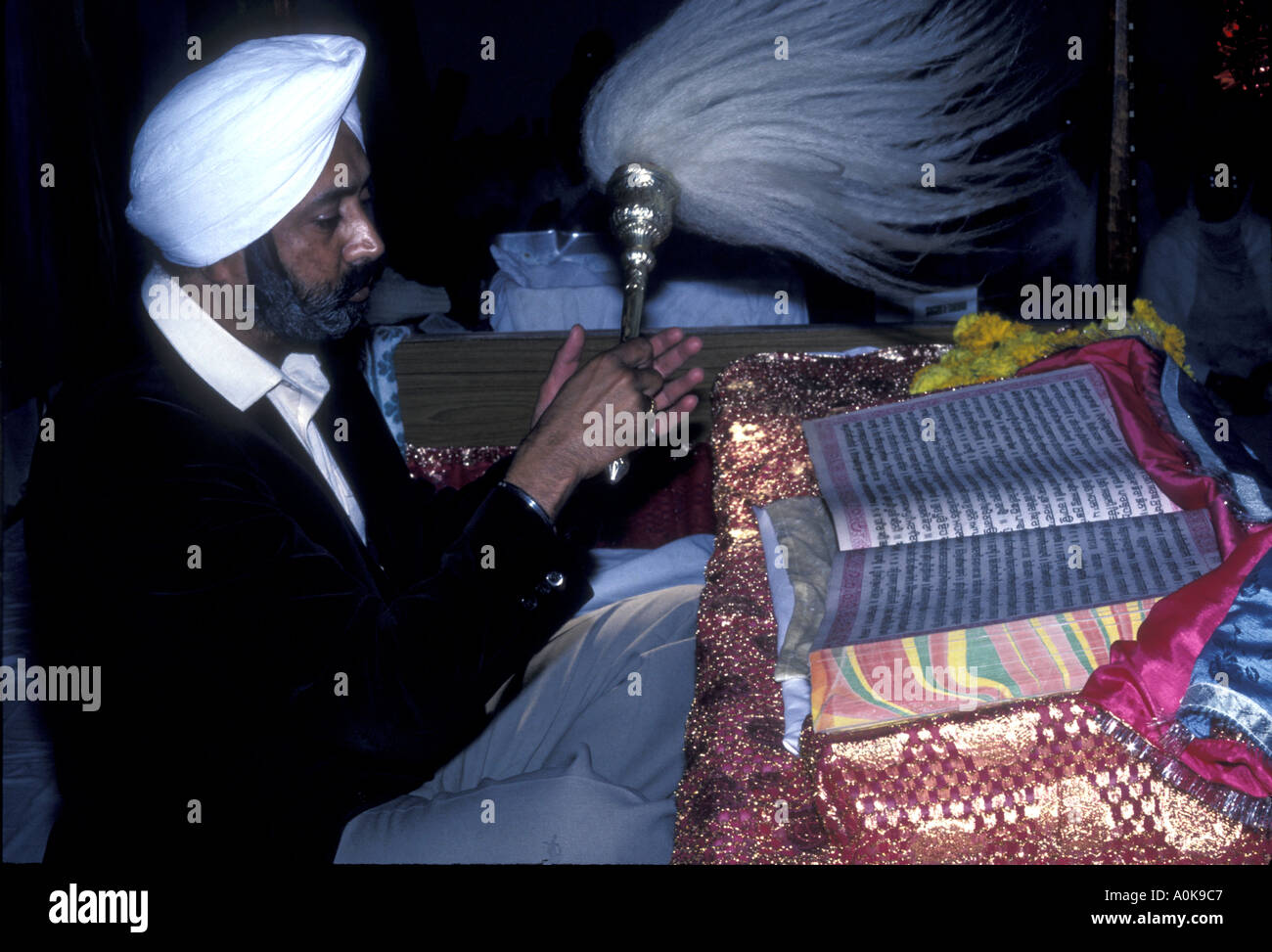 Ein männlicher Sikh, der die Chauri während des Gottesdienstes in einer Gurdwara über den heiligen Guru Granth Sahib winkt Stockfoto