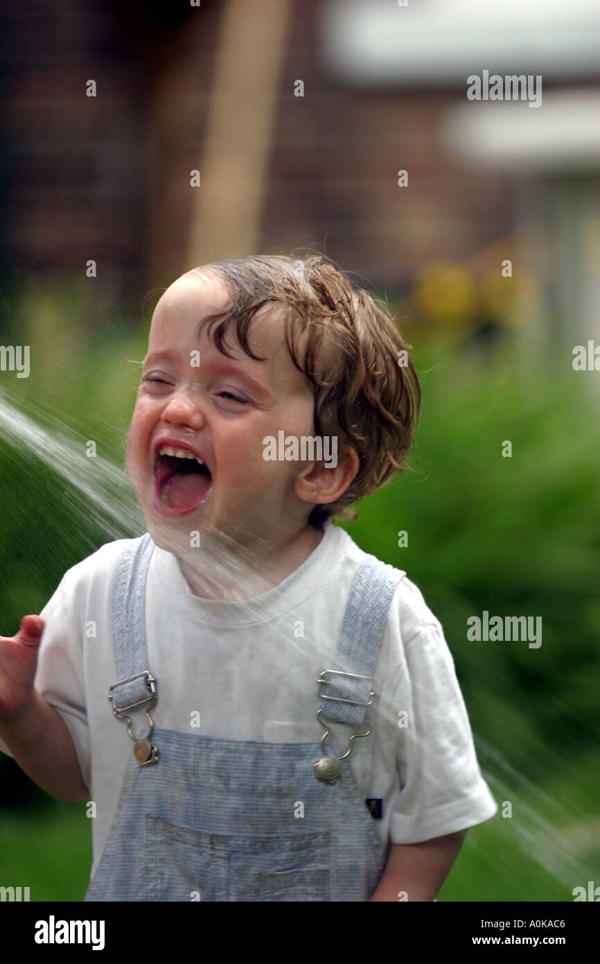 Lewis im Alter von zwei spielen mit dem Gartenschlauch im Garten Stockfoto