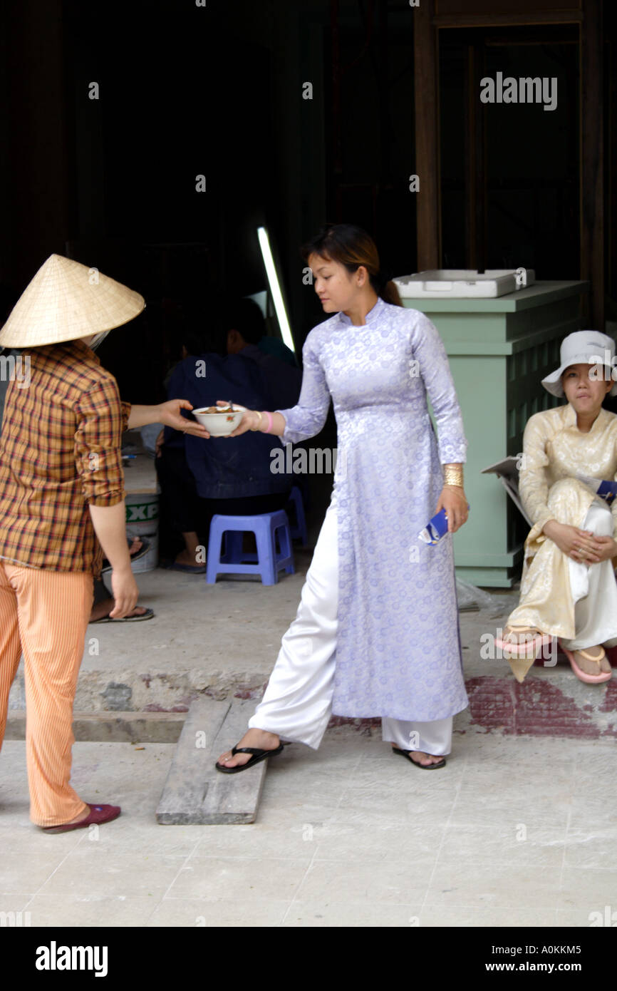 Frau in einem traditionellen Hut liefert Suppe an eine Frau in traditioneller Kleidung.   Saigon (HCMC) Vietnam Stockfoto