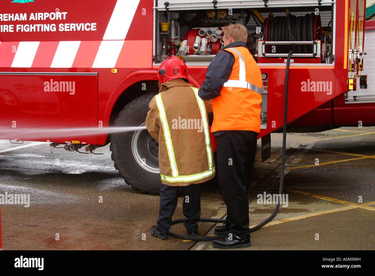 Feuerwehrmann zeigen junge Wasserschlauch Bedienung Stockfoto