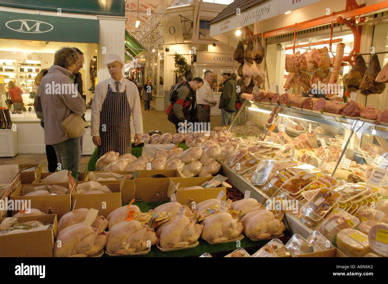 Last-Minute-Heiligabend-Shopper diskutieren Fleisch zum Verkauf vor Metzger laden in Oxfords bedeckt Markt Stockfoto