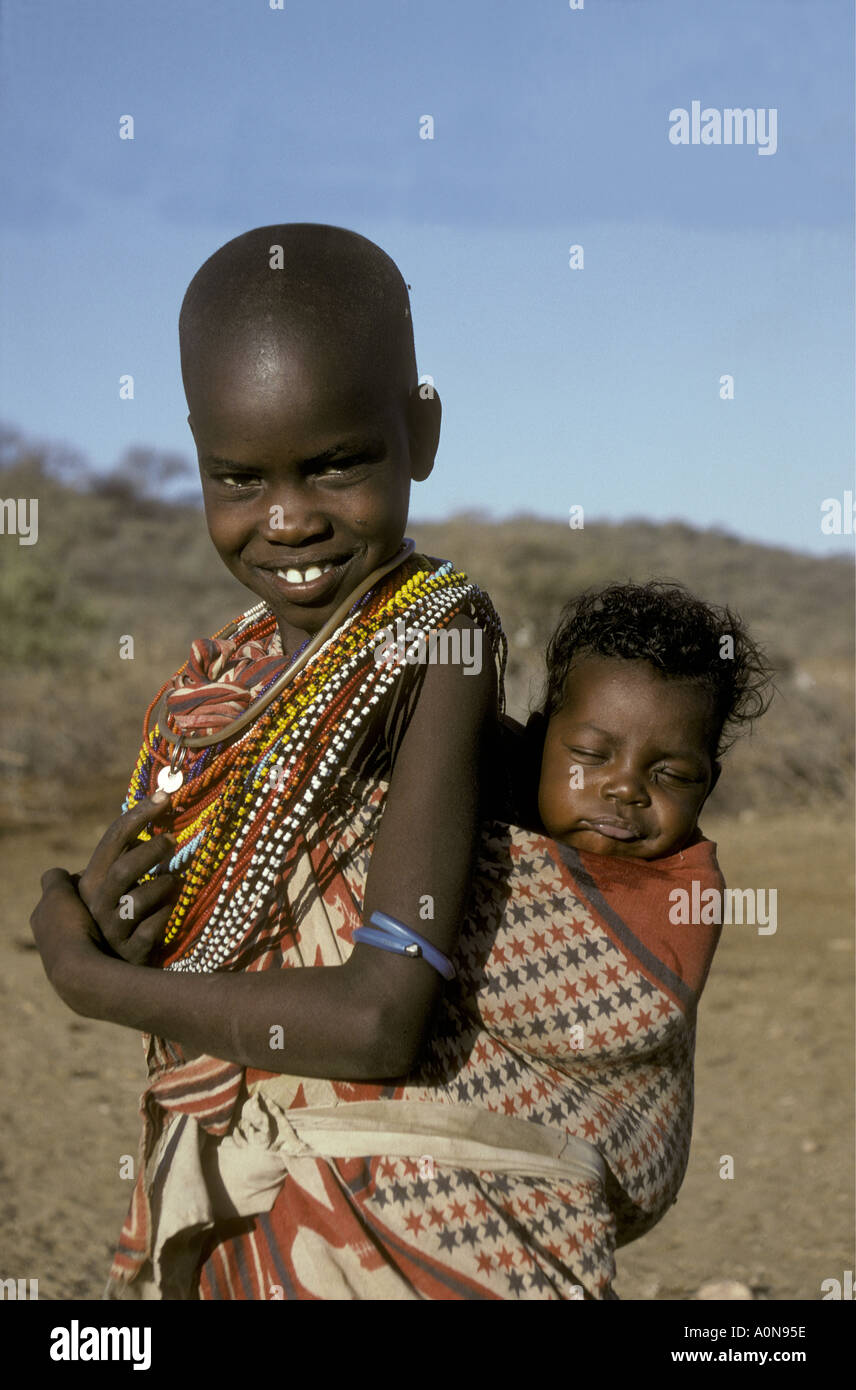 Eine Samburu Mädchen ca. 8 Jahre alten trägt ihre Babyschwester in einem Papoose Tuch auf ihr zurück in der Nähe von Samburu National Reserve Kenya Stockfoto