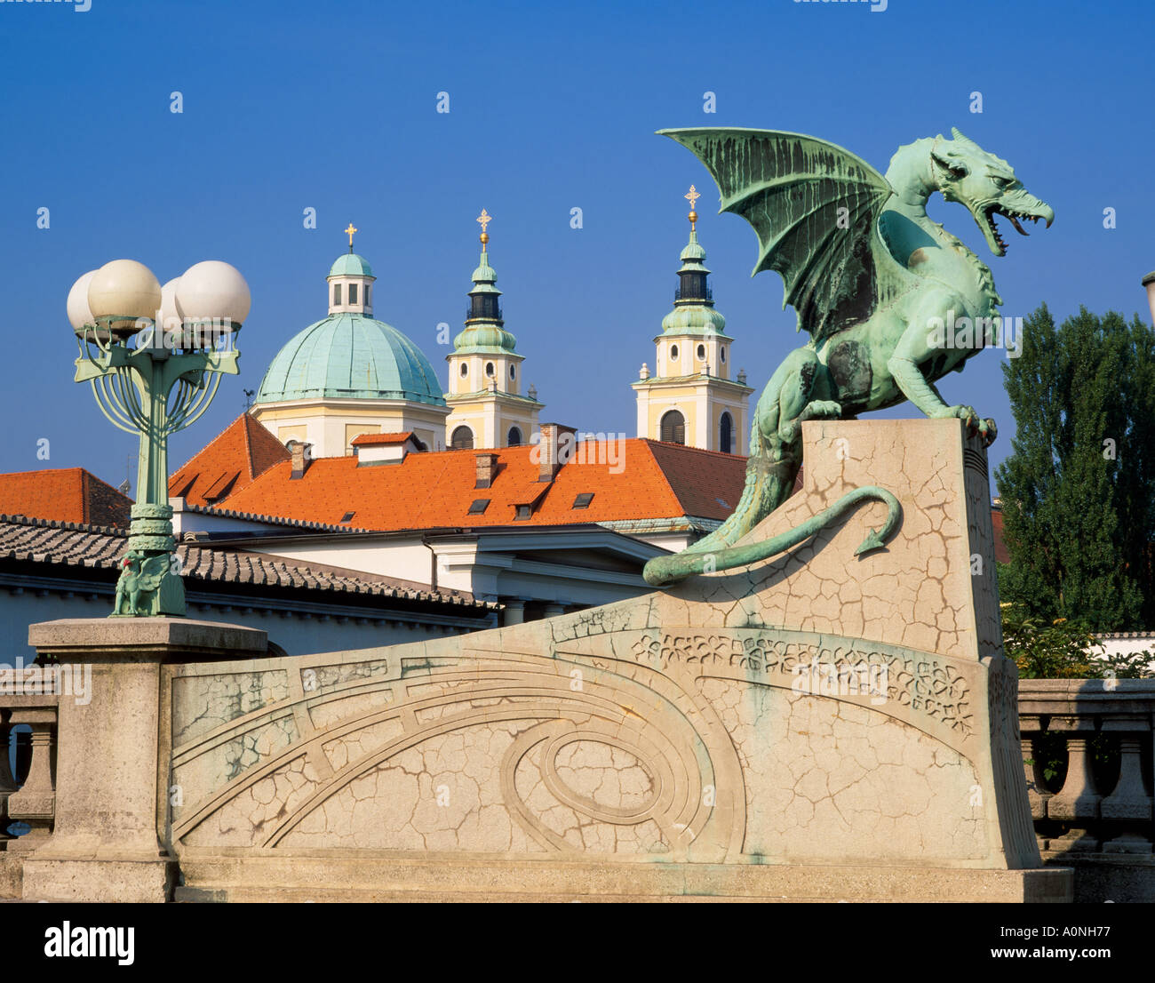 Einer der vier Drachen auf der Drachenbrücke, Ljubljana, Slowenien.  Hinten sind die Türme der Kathedrale von St. Nikolaus Stockfoto
