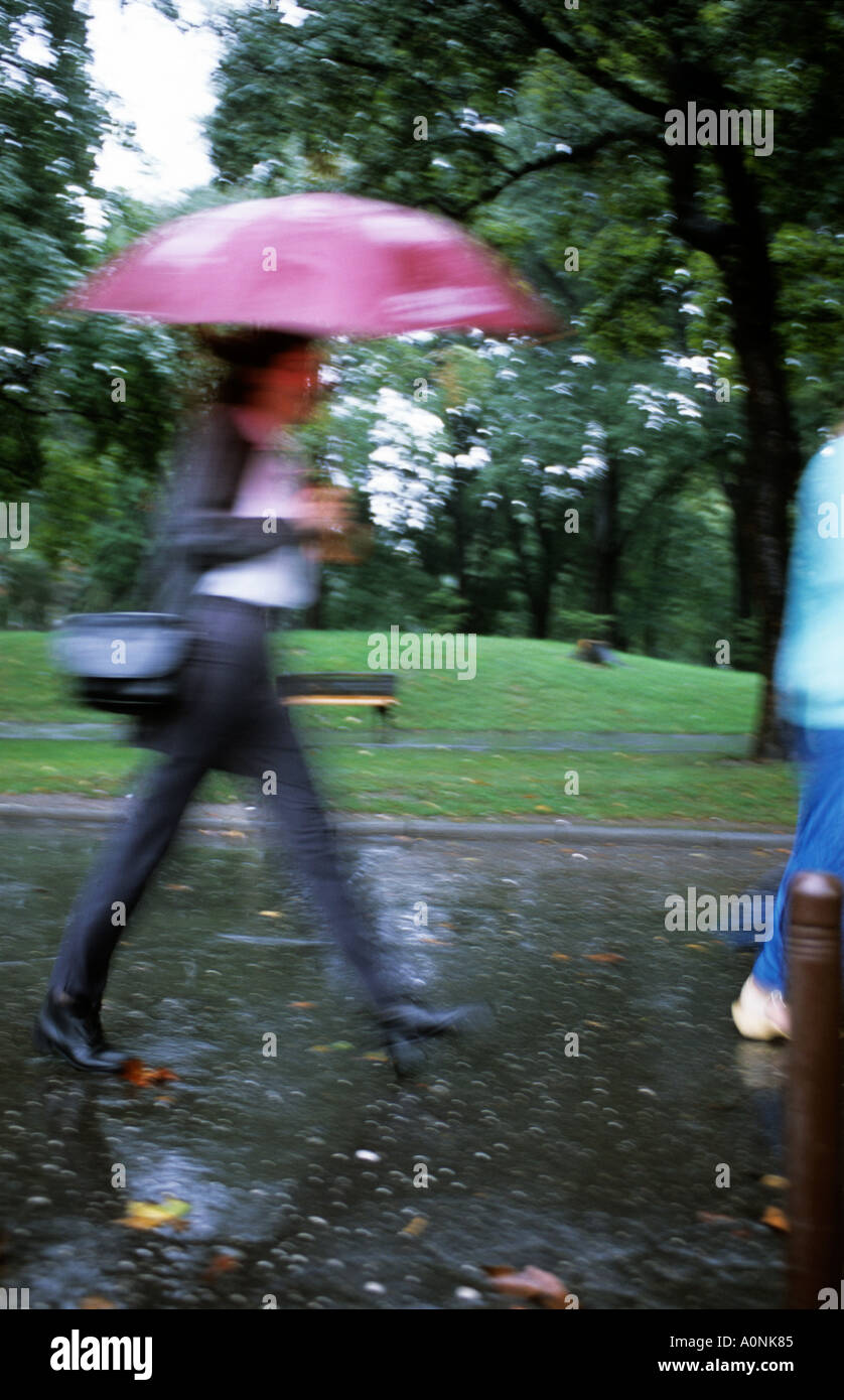 Belgrad, Serbien, Jugoslawien. Modebewusste junge Frau im Regen mit Regenschirm marschieren durch einen Park; Bewegungsunschärfe. Stockfoto