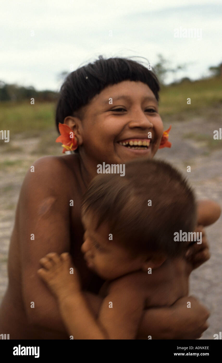 Roraima, Brasilien. Lachend Yanomami Frau mit Blume Ohr Stecker hält ihr Kind. Stockfoto